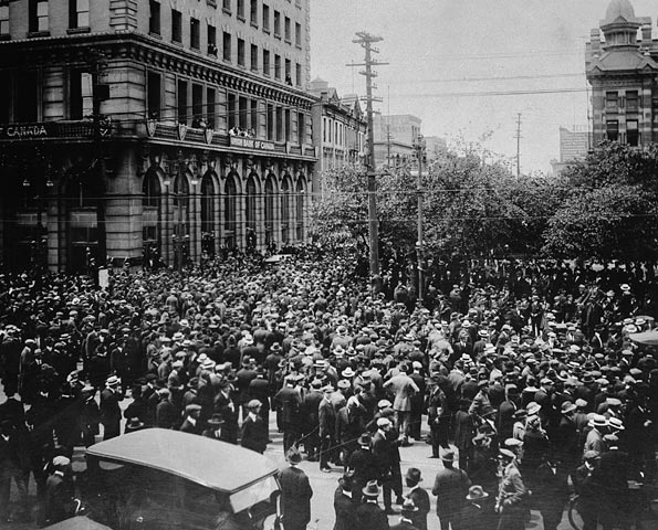Black and white image of thousands of workers standing outside the city hall in Winnipeg standing at a crowded intersection.