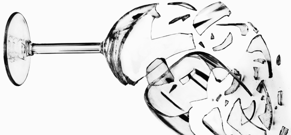 A b/w image of a wine glass on its side with the bowl end shattering into tiny pieces.