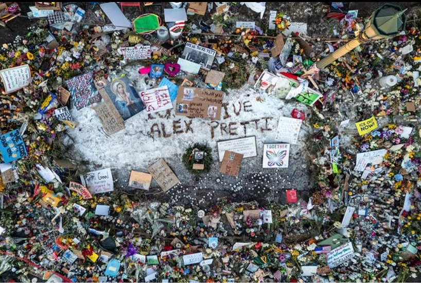 Looking down at the pavement memorial to Alex Pretti, spelled out in little sticks it says "Long Live Alex Pretti." Flowers, candles, and cards flow out from all directions.